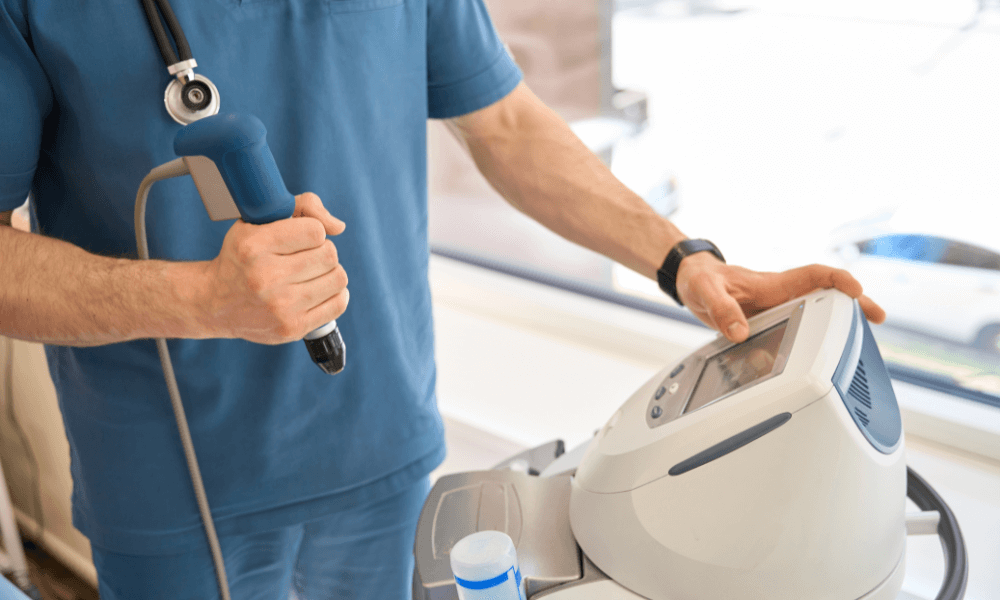 Can Shockwave Therapy Help With Plantar Fasciitis A medical professional holding a device in one hand and adjusting a machine with the other, in a clinical setting.